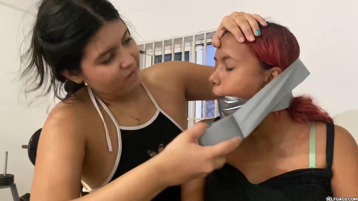No Pain, No Gain: An Intense Day of Fitness, Discipline and Gags at Mary's Training Camp Two girls named Penelopé Garcia and Barby Luna are sent to a training camp by their step-parents, where they meet their strict trainer Mary. As soon as they enter the gym room, Mary gives them instructions to sit on the floor. Mary is wearing high heeled shoes, a black dress, and some pantyhose. Penelopé and Barby are wearing dresses, pantyhose, socks, and shoes, with their hair in pigtails.<br><br>Mary is a no-nonsense trainer and immediately shows her authority by throwing Barby a red ball gag, instructing her to put it in her mouth and lock it tight. She then throws a roll of silver duct tape to Penelopé and tells her to tape her mouth shut. Mary tells the girls not to talk or complain in her class, and she makes them run on the spot, do jumping jacks and squads for about 3 minutes!<br><br>After this, Mary makes Barby sit on the bike, while Penelopé goes to the machine. She instructs them to start exercising, and Mary constantly watches them, telling them to go faster and not to stop. If Barby starts drooling, it would be nice. The exercise goes on for about 2 minutes, and then Mary tells the girls to swap positions!<br><br>Penelopé goes on the bike, and Barby on the machine. The exercise continues for another 2 minutes. Penelopé is exhausted after using the bike, and she takes the tape off her mouth, asking Mary to stop. Mary gets angry at Penelopé for taking off her gag and tells her to sit down on the floor. Mary then removes both of Barby's shoes and socks, and stuffs both socks into Penelopé's mouth, wrapping silver duct tape around her head as a really tight gag!<br><br>"For that behavior, you will now get 2 more minutes on the bike! Let's go!" Mary yells at Penelopé (in Spanish). She instructs Barby to stand up and run on the spot while Penelopé goes back on the bike!<br><br>After 2 more minutes, Mary tells the girls to stop and take a 30-minute break. Mary ties up Barby's and Penelopé's hands in front of them with some rope and takes them outside, where she ties their arms up exactly like this next to each other!<br><br>"You can stay here to refresh yourself now. See you again in 30 minutes!" Mary says (in Spanish) as she leaves the girls to struggle, walk around, and squirm. Penelopé and Barby are nervous and scared about what Mary might do next. They wonder if they will survive the training camp, and if they will be able to escape Mary's strict rules!